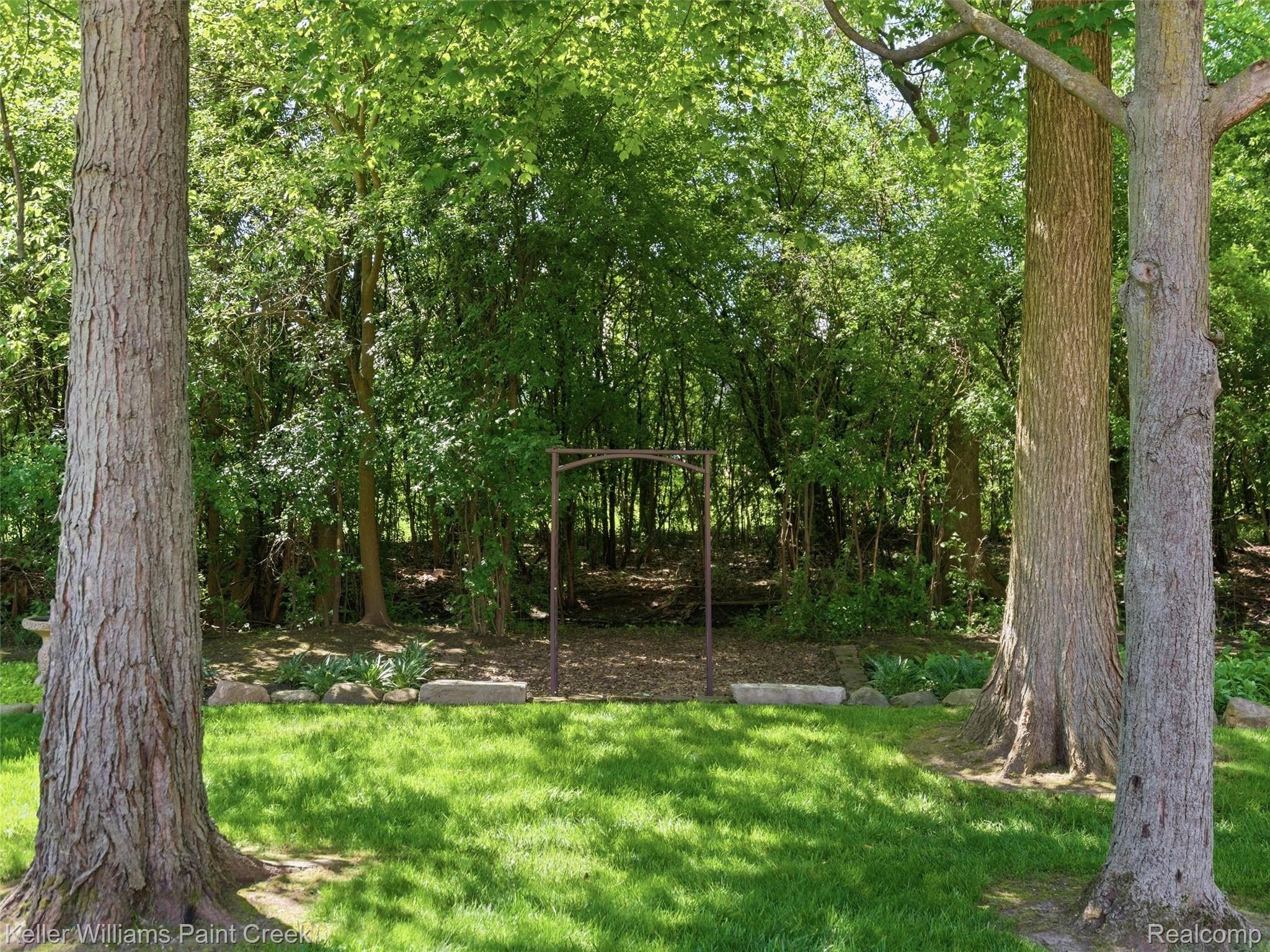 2842 Manorwood Road Troy, MI 48085 - Photo 68 of 72 Expansive grassy area featuring mature trees, a metal archway, and natural landscaping with stones and foliage