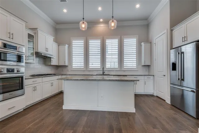 a kitchen with stainless steel appliances granite countertop a refrigerator a sink dishwasher a stove and white countertops with wooden floor