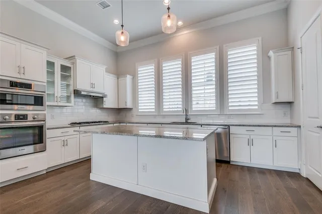a kitchen with stainless steel appliances granite countertop white cabinets a sink a window and wooden floor