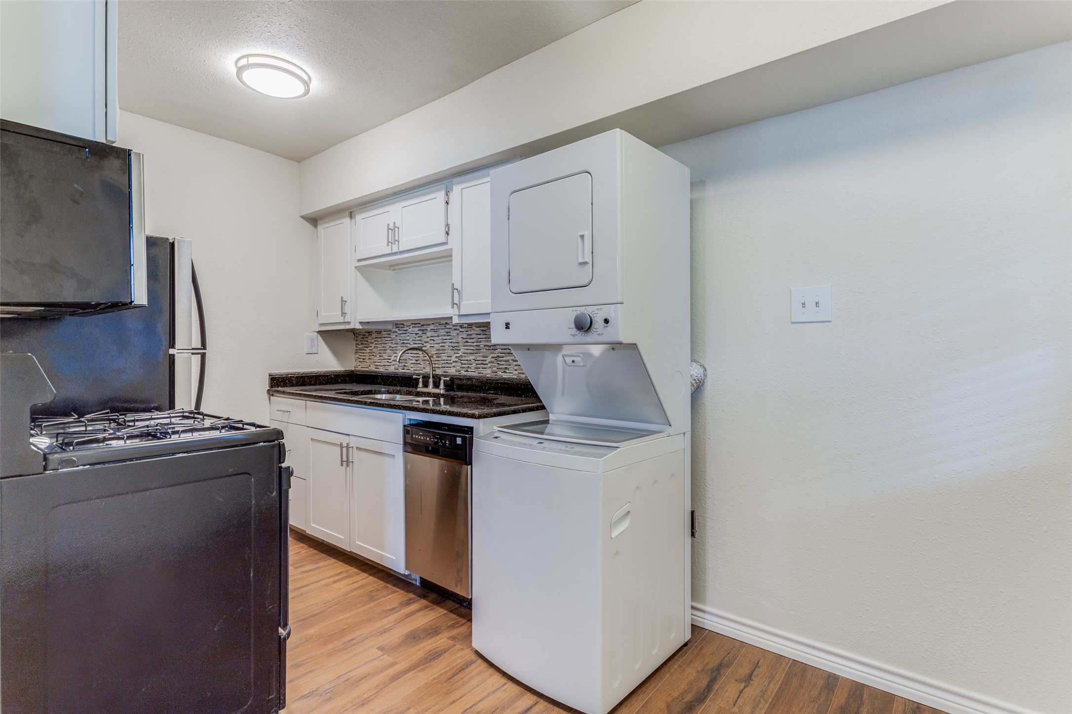 2401 Manor Road, Unit 113 Austin, TX 78722 - Photo 5 of 12 Kitchen featuring appliances with stainless steel finishes, stacked washer / drying machine, baseboards, decorative backsplash, and light wood-style floors