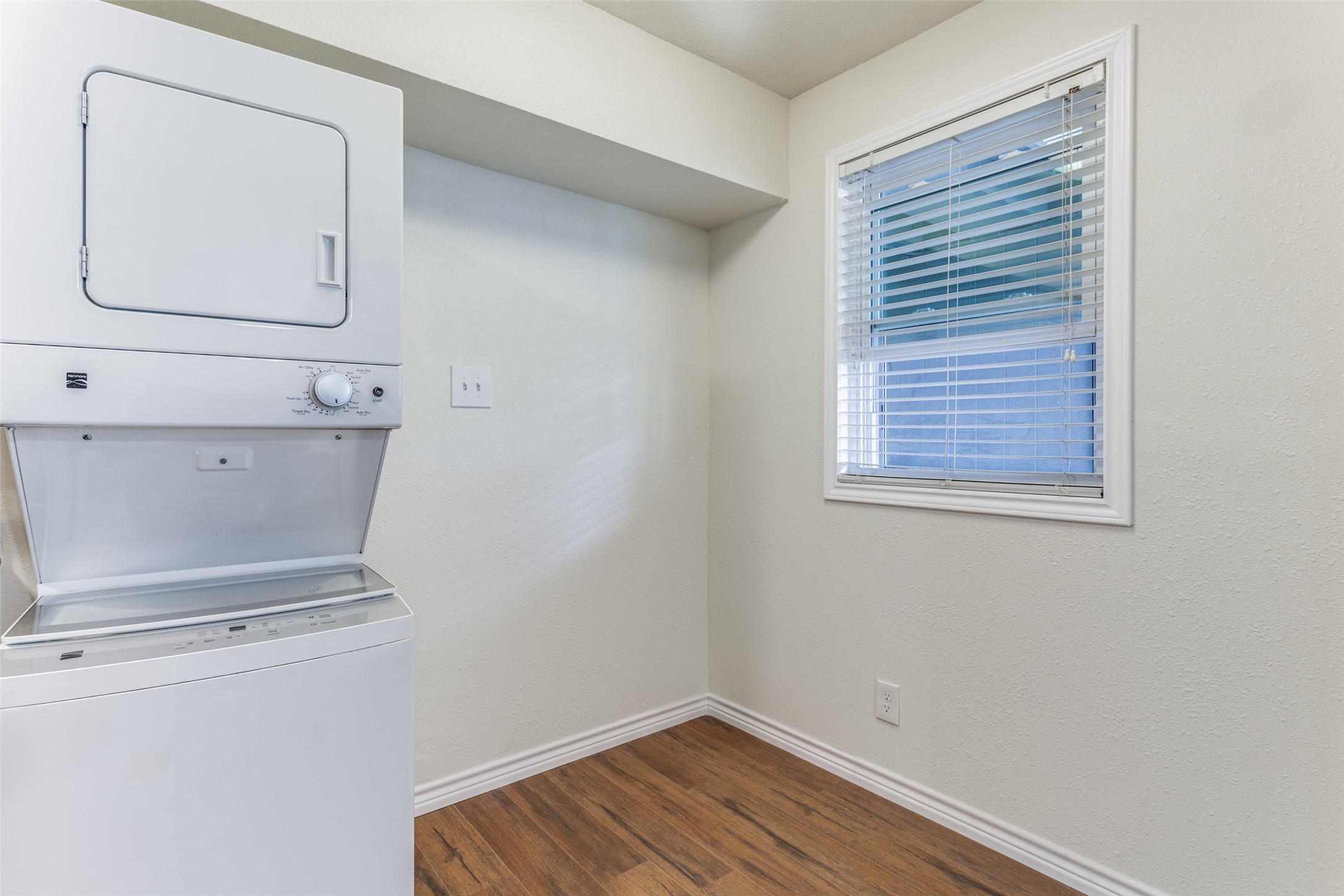 2401 Manor Road, Unit 113 Austin, TX 78722 - Photo 9 of 12 Laundry room with estacked washer and dryer, dark wood-style flooring, and baseboards