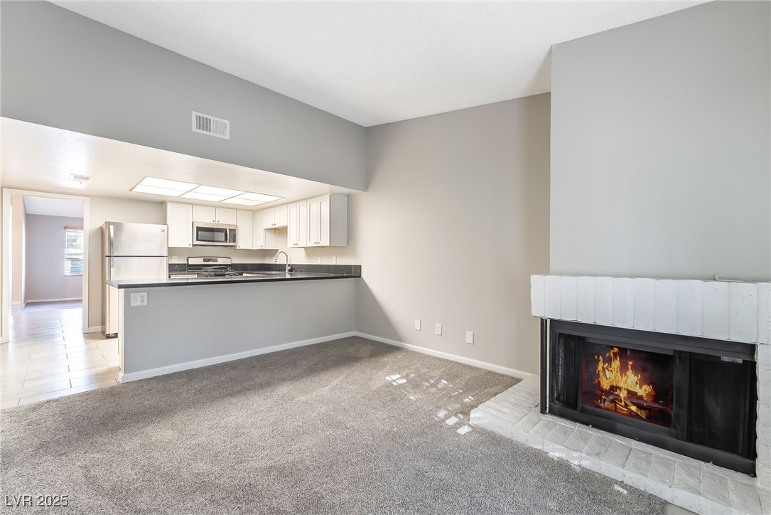 2755 Carnation Lane Henderson, NV 89074 - Photo 18 of 42 Unfurnished living room with light colored carpet, light tile patterned flooring, and a brick fireplace