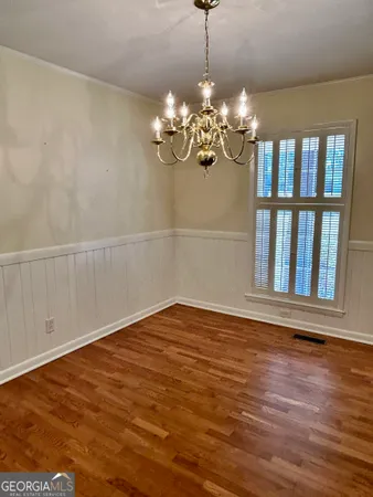 a view of an empty room with chandelier and wooden floor