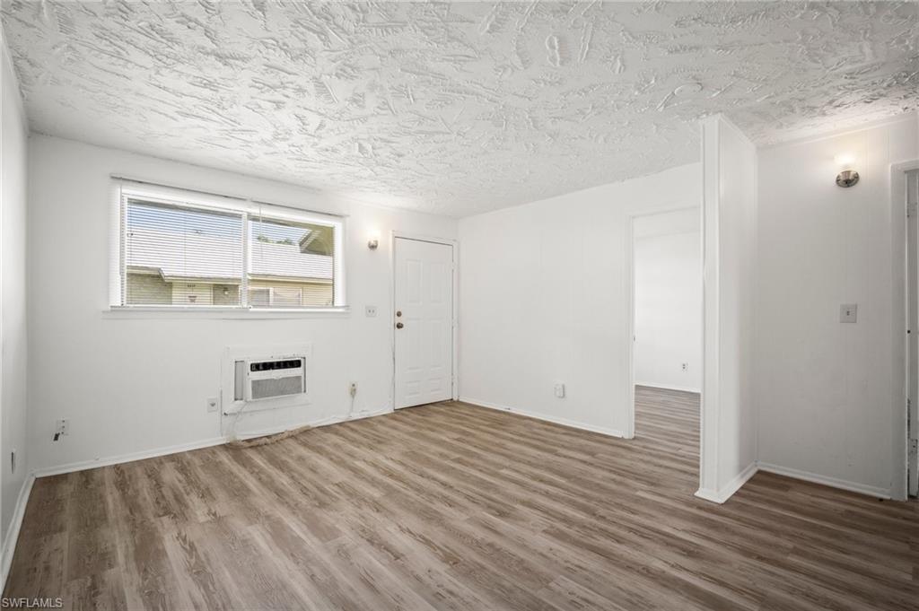 3215 Jeffcott Street Fort Myers, FL 33916 - Photo 13 of 33 Unfurnished living room with an AC wall unit, wood finished floors, and a textured ceiling
