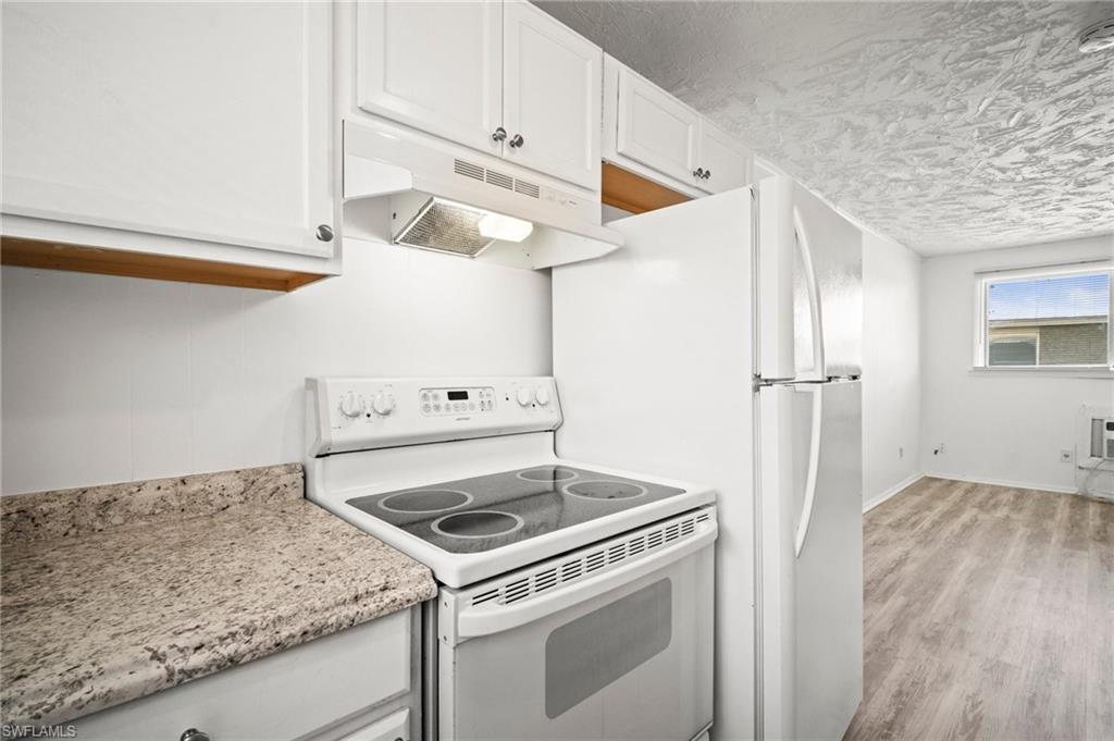 3215 Jeffcott Street Fort Myers, FL 33916 - Photo 16 of 33 Kitchen with white appliances, under cabinet range hood, white cabinetry, light wood-type flooring, and a textured ceiling