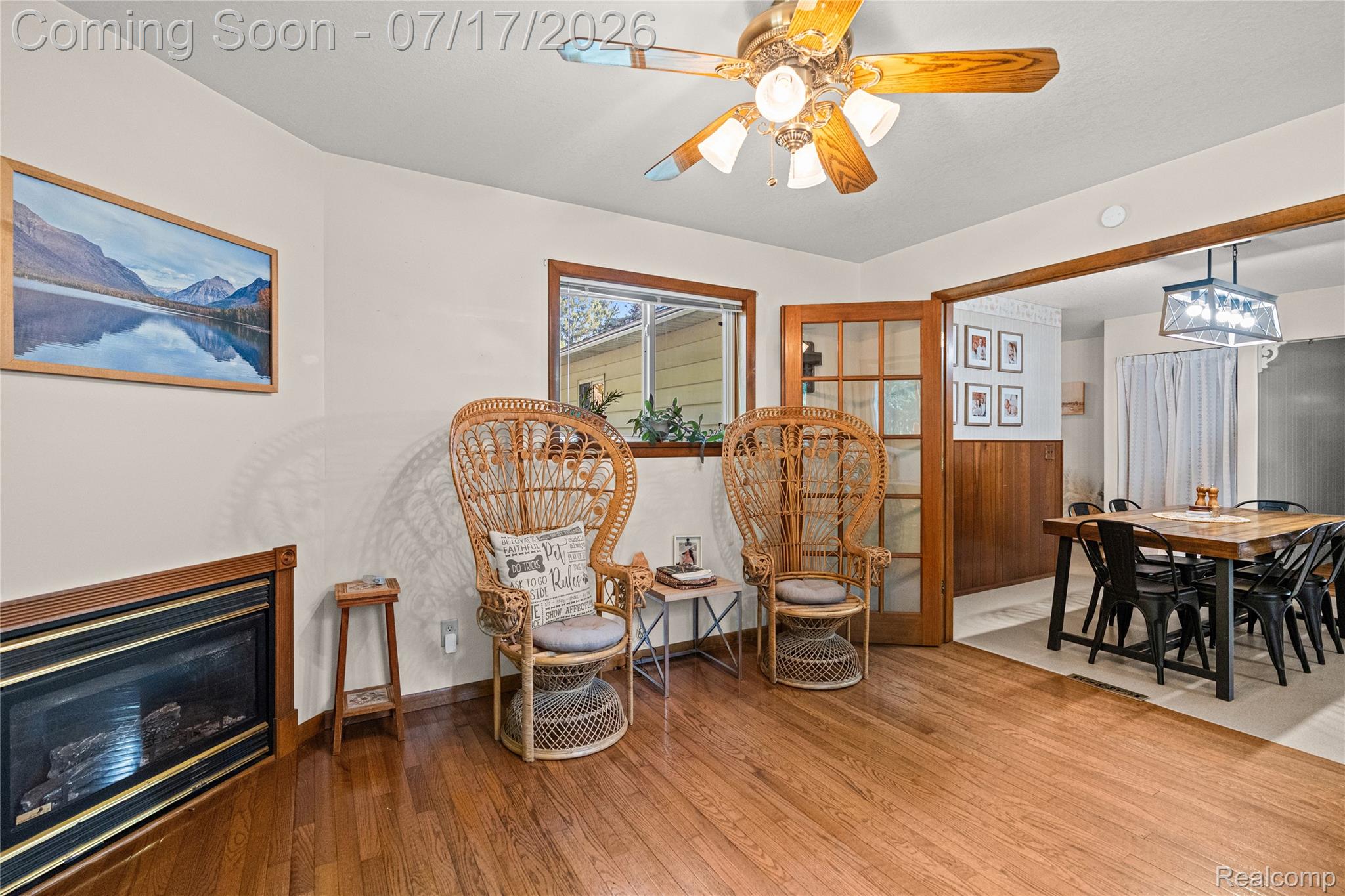 11255 North Center Road Clio, MI 48420 - Photo 17 of 37 Hardwood flooring extending into an adjacent dining area, featuring a built-in fireplace with a gold-trimmed surround, a ceiling fan with integrated lighting, and a window with wood trim