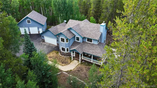 an aerial view of a house with yard and trees in the background
