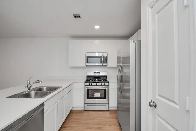a kitchen with stainless steel appliances a refrigerator a sink and white cabinets