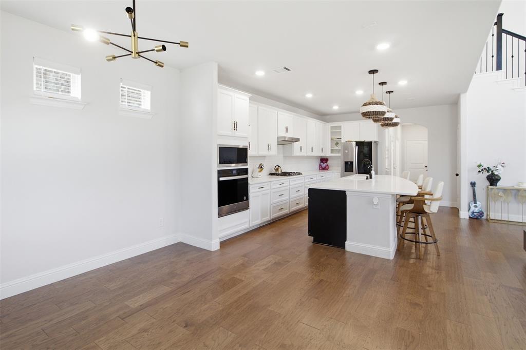 7416 Sequoia Rdg Road Little Elm, TX 76227 - Photo 9 of 37 Open-concept kitchen and dining area featuring wood-finish flooring, white cabinetry, integrated stainless steel appliances, a center island with countertop seating, and a contemporary chandelier