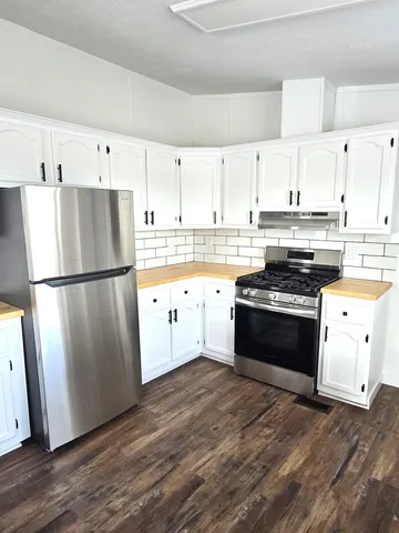 a kitchen with granite countertop a refrigerator stove and white cabinets