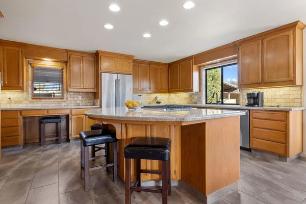 a kitchen with granite countertop wooden cabinets a stove a sink dishwasher and a refrigerator with wooden floor