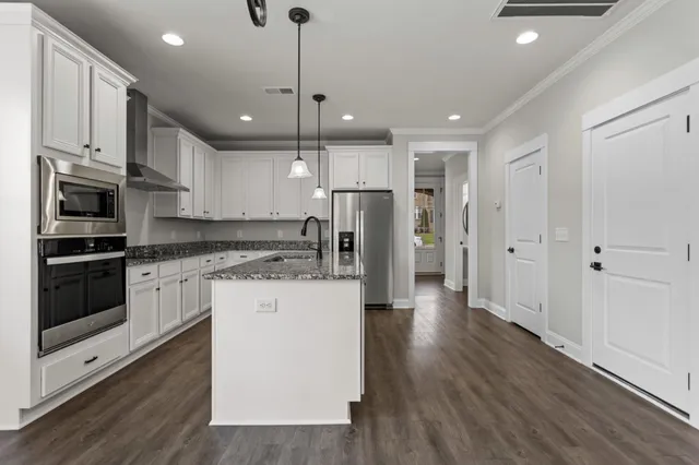 a kitchen with stainless steel appliances kitchen island granite countertop a refrigerator a oven a sink and white cabinets with wooden floor