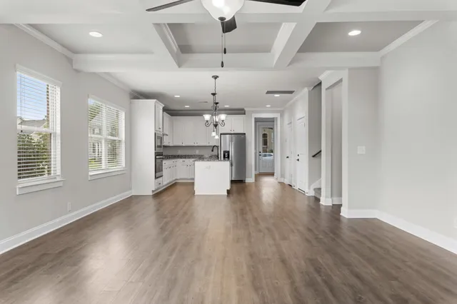 a view of an empty room and kitchen with wooden floor