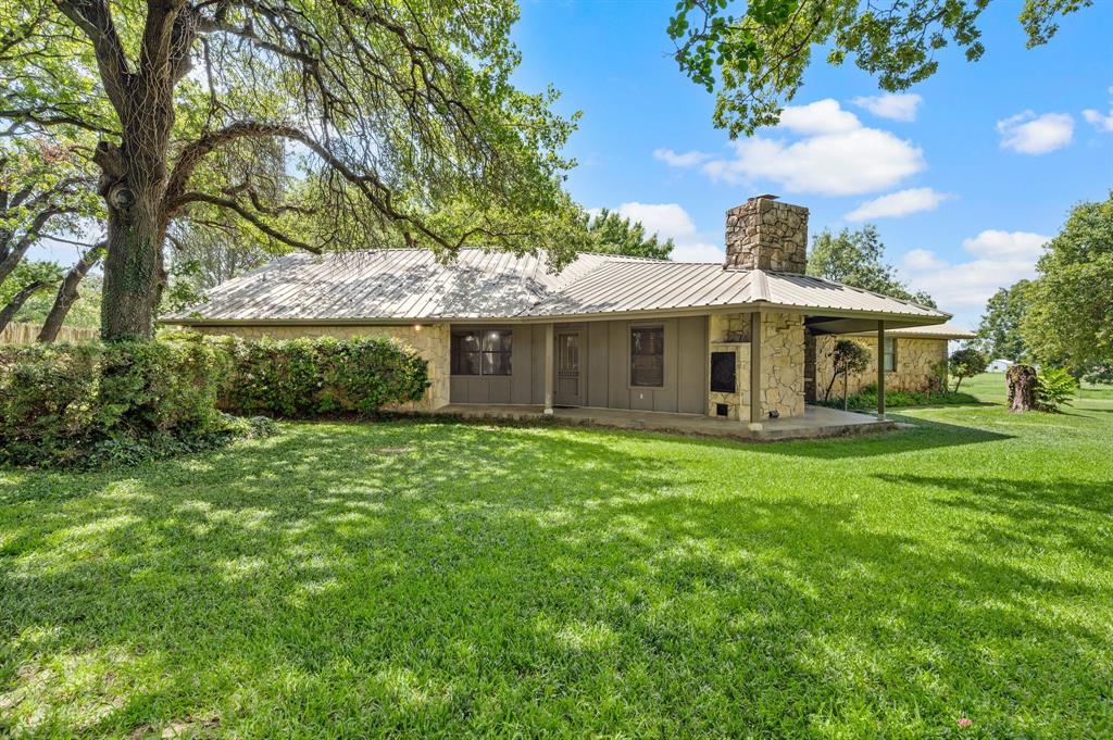 515 New Highland Road Springtown, TX 76082 - Photo 23 of 38 Stone exterior residence featuring a covered patio, metal roof, and an exterior stone fireplace