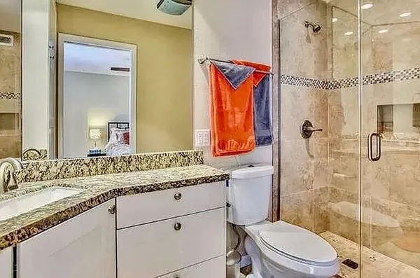 a bathroom with a granite countertop sink a mirror a toilet and shower