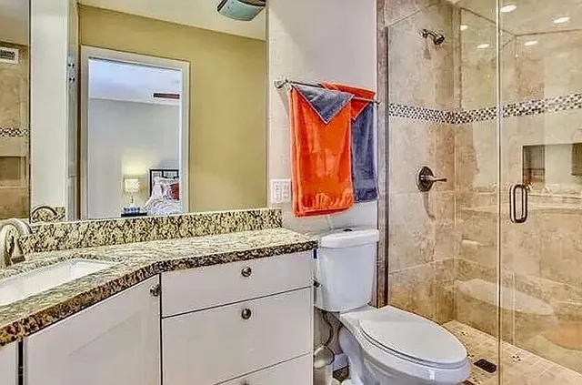 a bathroom with a granite countertop sink a mirror a toilet and shower