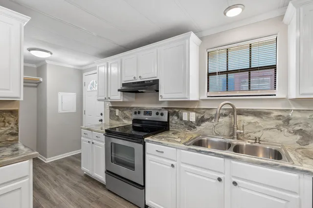 a kitchen with stainless steel appliances granite countertop white cabinets a sink a stove a microwave and a window