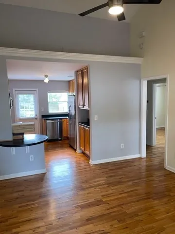 an empty room with wooden floor kitchen view and windows
