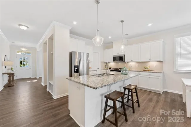 a kitchen with stainless steel appliances kitchen island granite countertop a stove a sink a refrigerator and white cabinets with wooden floor