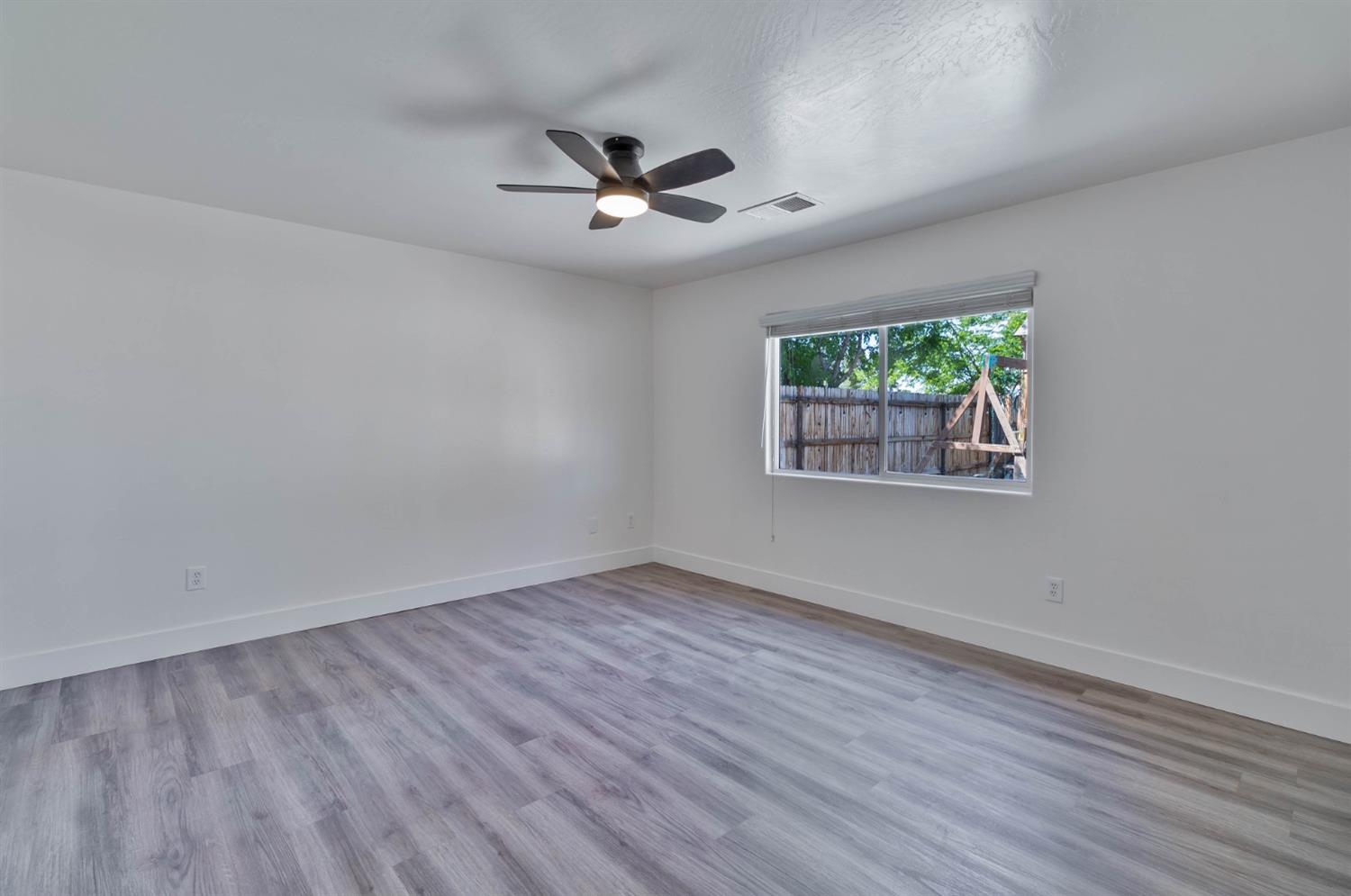 7110 Firebaugh Street Bakersfield, CA 93313 - Photo 13 of 37 an empty room with wooden floor chandelier fan and windows
