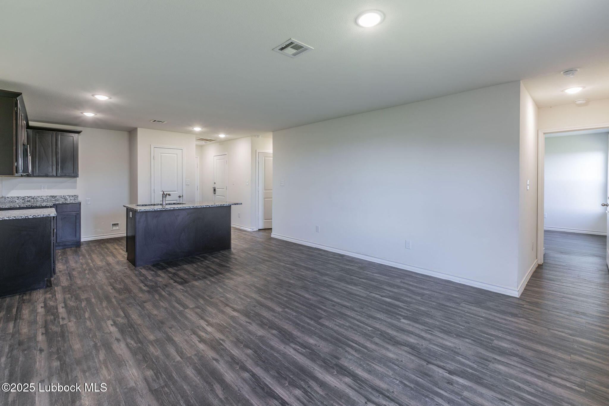 3511 East Colgate Street Lubbock, TX 79403 - Photo 3 of 18 a view of an empty room with wooden floor and a kitchen