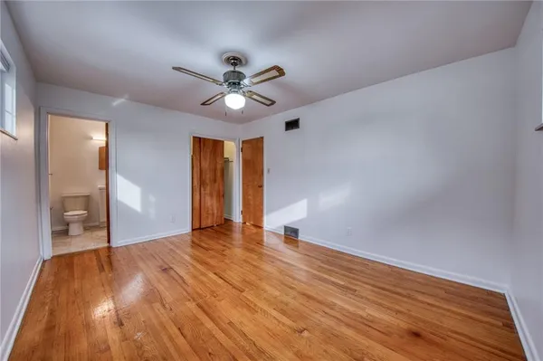 a view of an empty room with wooden floor and a ceiling fan