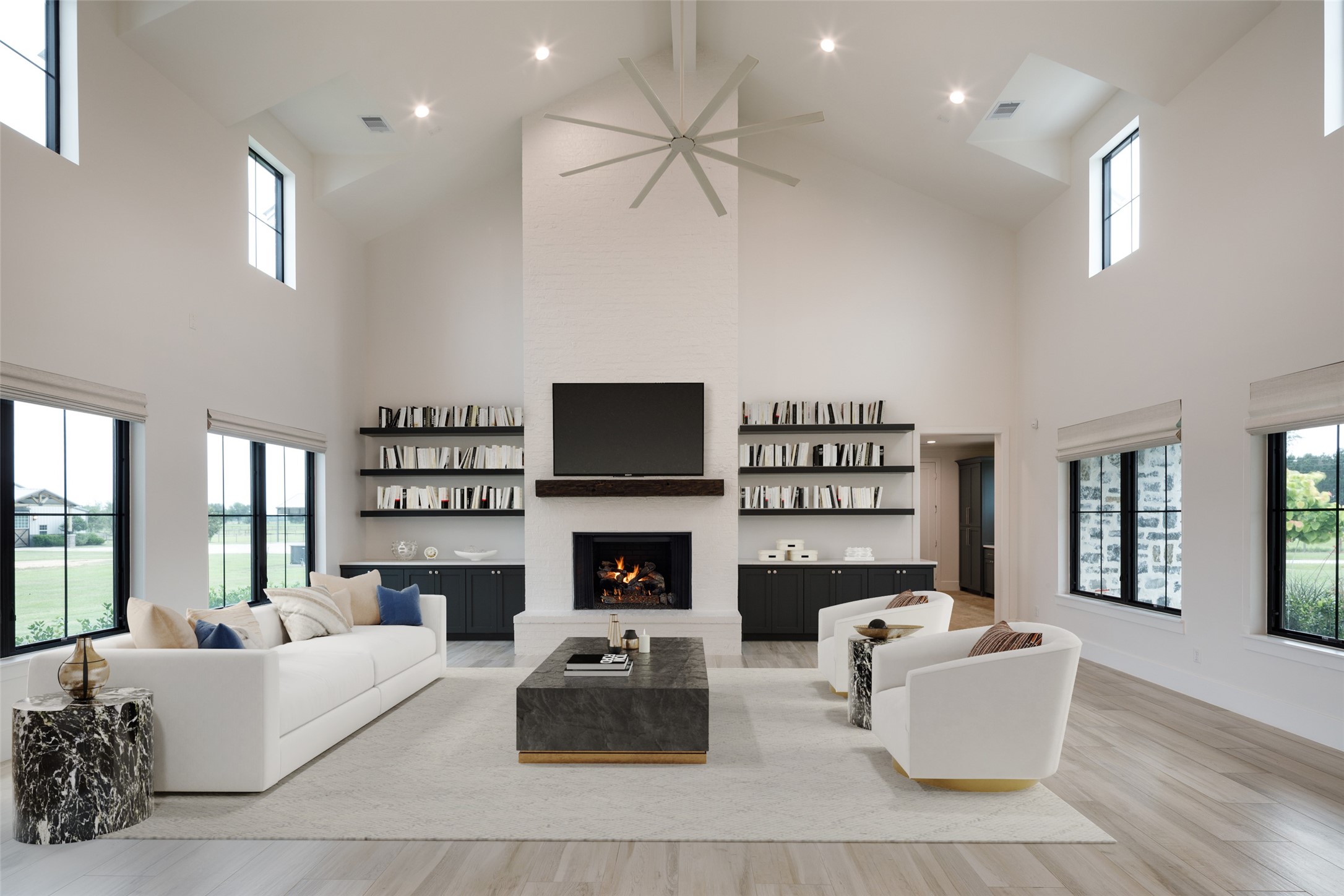 24118 Margerstadt Road Hockley, TX 77447 - Photo 17 of 46 A vaulted ceiling with an oversized statement fan anchors the main living area, while custom built-ins and the fireplace create definition within the open layout. Expansive window lines keep the surrounding pasture visible throughout the space without sacrificing warmth or intimacy.