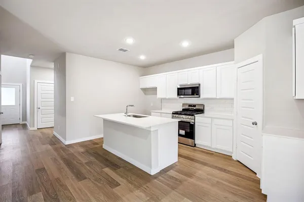 a kitchen with stainless steel appliances white cabinets a sink a stove a microwave and a refrigerator