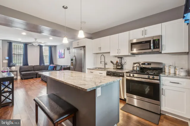 a kitchen with stainless steel appliances kitchen island granite countertop a stove top oven a sink dishwasher a dining table and chairs with wooden floor