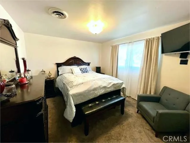 a spacious bedroom with a bed and a flat tv screen on dresser