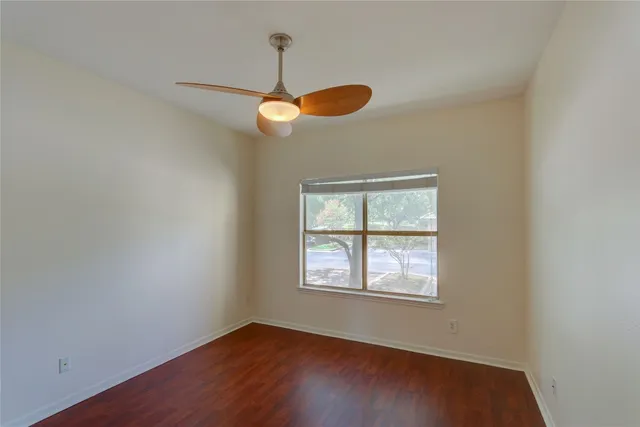 an empty room with wooden floor chandelier fan and windows