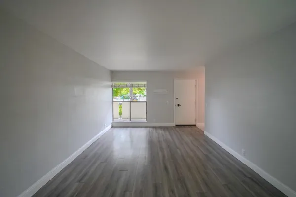 a view of an empty room with wooden floor and a window