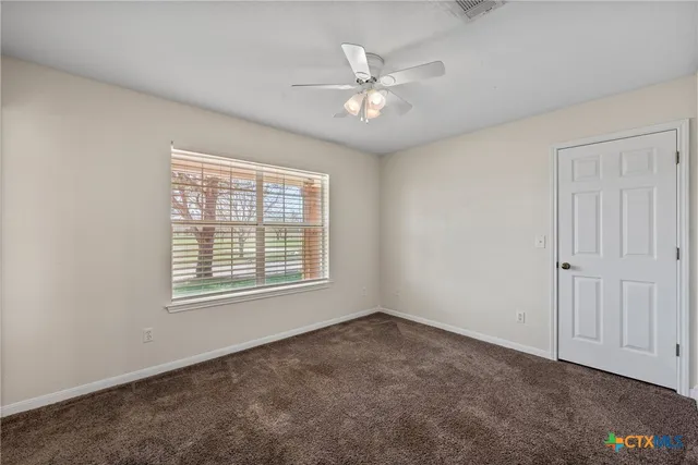 a view of an empty room with window and chandelier fan