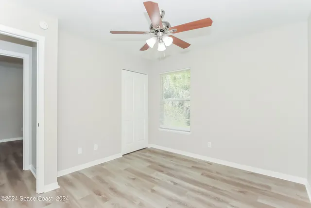an empty room with wooden floor fan and windows
