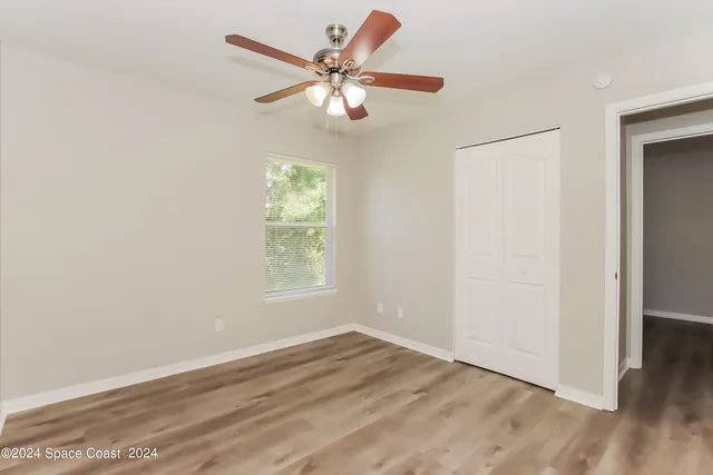 an empty room with wooden floor fan and windows