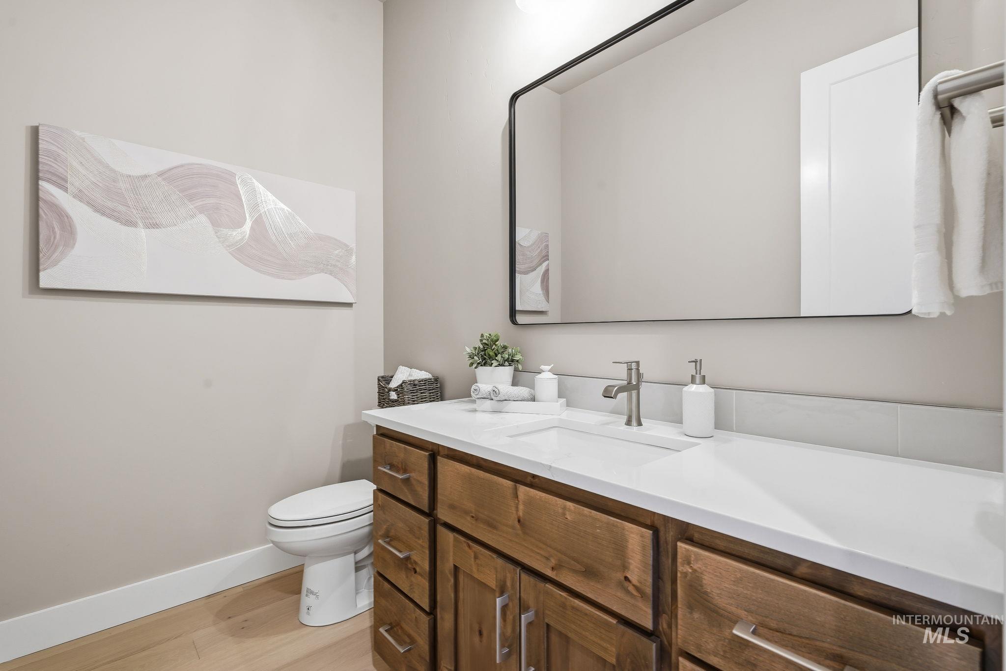 470 South Radiator Way Boise, ID 83716 - Photo 44 of 50 Bathroom featuring a wood-finish vanity with a white countertop, an integrated sink, a rectangular black-framed mirror, and wood-finish flooring