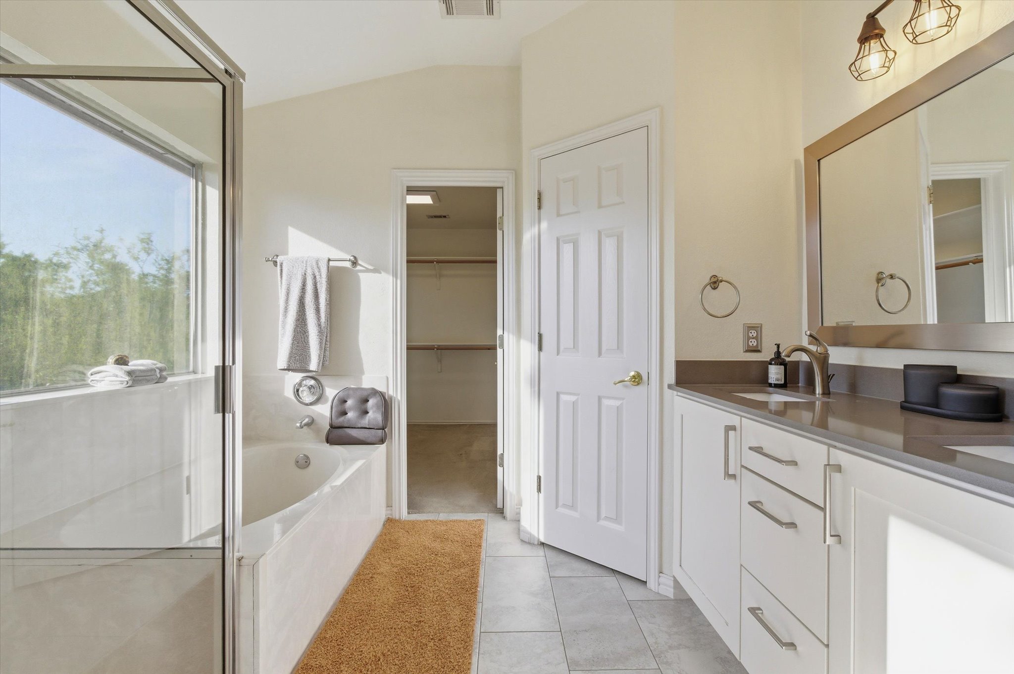 8920 West Hove Loop Austin, TX 78749 - Photo 14 of 39 Bathroom featuring a built-in tub with a window, glass-enclosed shower, dual vanity with a built-in sink, framed mirror, and tiled flooring