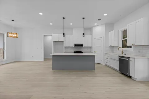 a large kitchen with stainless steel appliances kitchen island granite countertop a large counter top a stove a sink dishwasher and a refrigerator with white cabinets