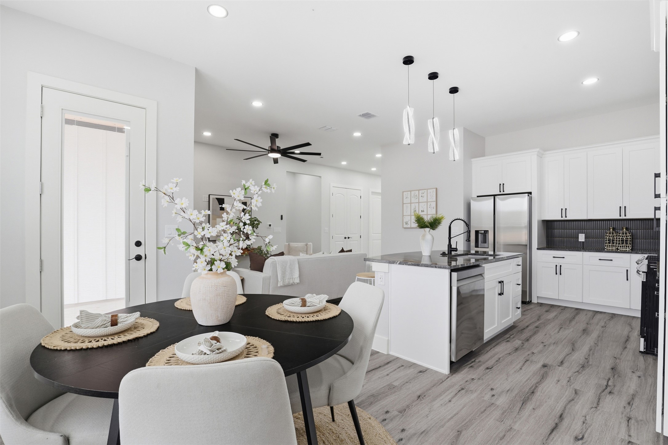 113 Los Robles Road Elgin, TX 78621 - Photo 5 of 20 Modern kitchen and dining area featuring wood-finish flooring, white cabinetry, a dark tiled backsplash, stainless steel appliances, and an island with pendant lighting