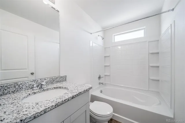 a bathroom with a granite countertop bathtub shower sink vanity and toilet