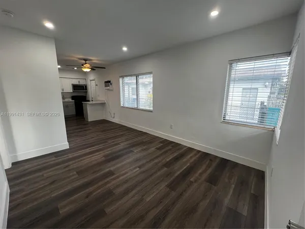 an empty room with wooden floor kitchen view and windows