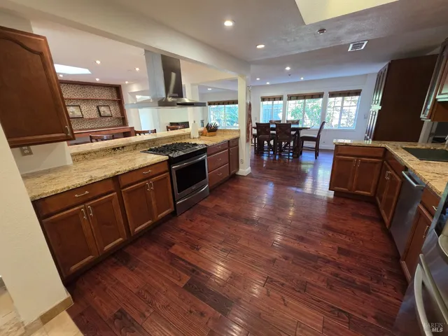 a large kitchen with stainless steel appliances granite countertop wooden floors and a view of living room