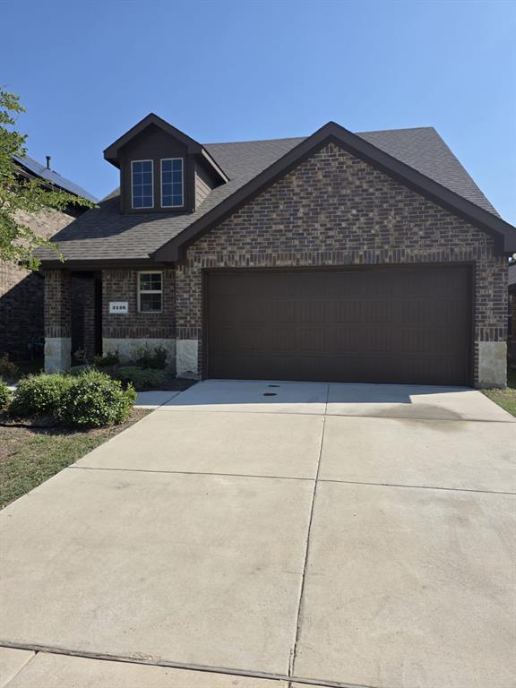 View of front of house with a shingled roof, brick siding, driveway, and a garage