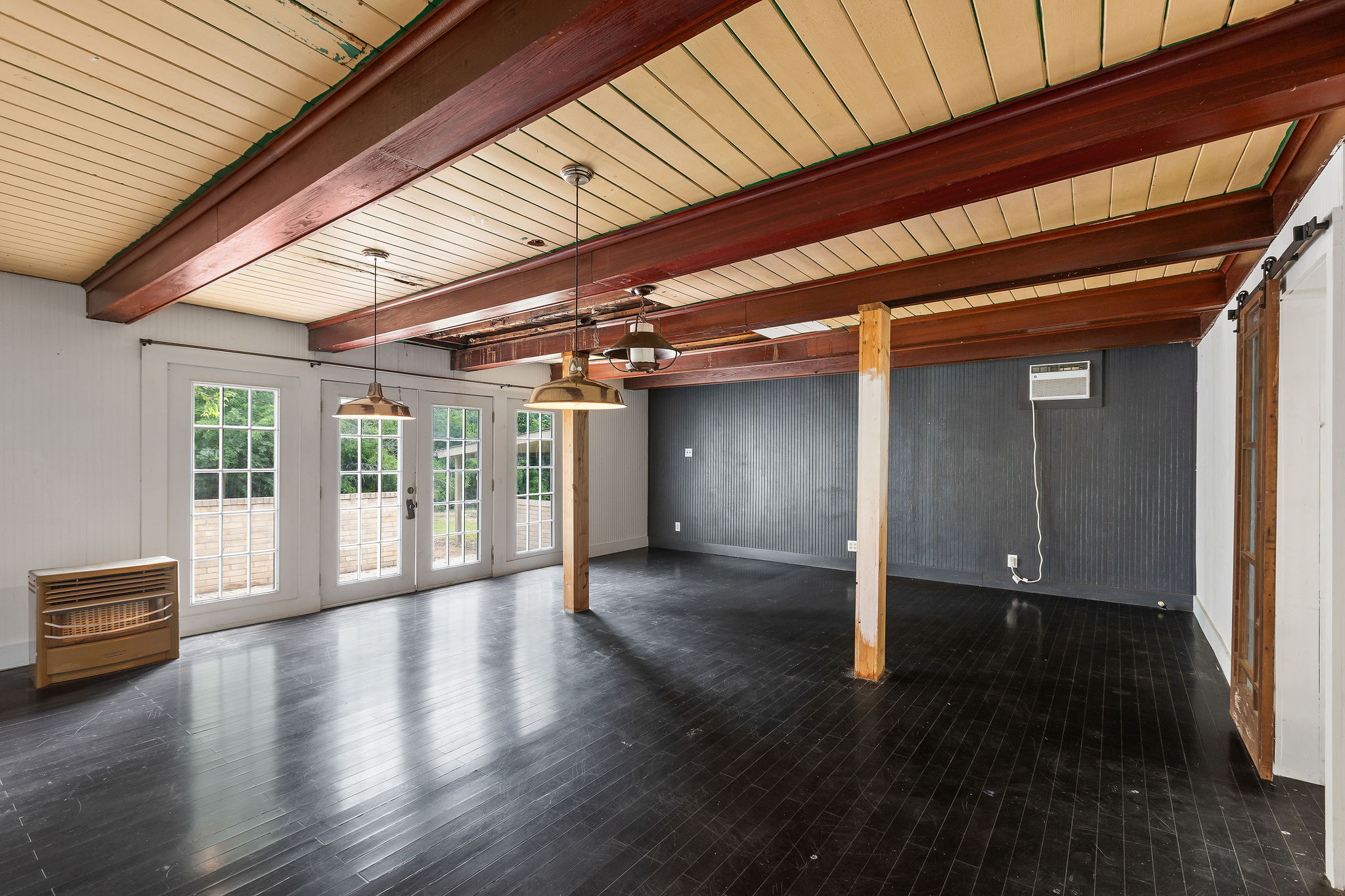 948 Maple Street Lockhart, TX 78644 - Photo 14 of 40 Bold black flooring and exposed wood beams define this versatile living space, opening to the outdoors through French doors.
