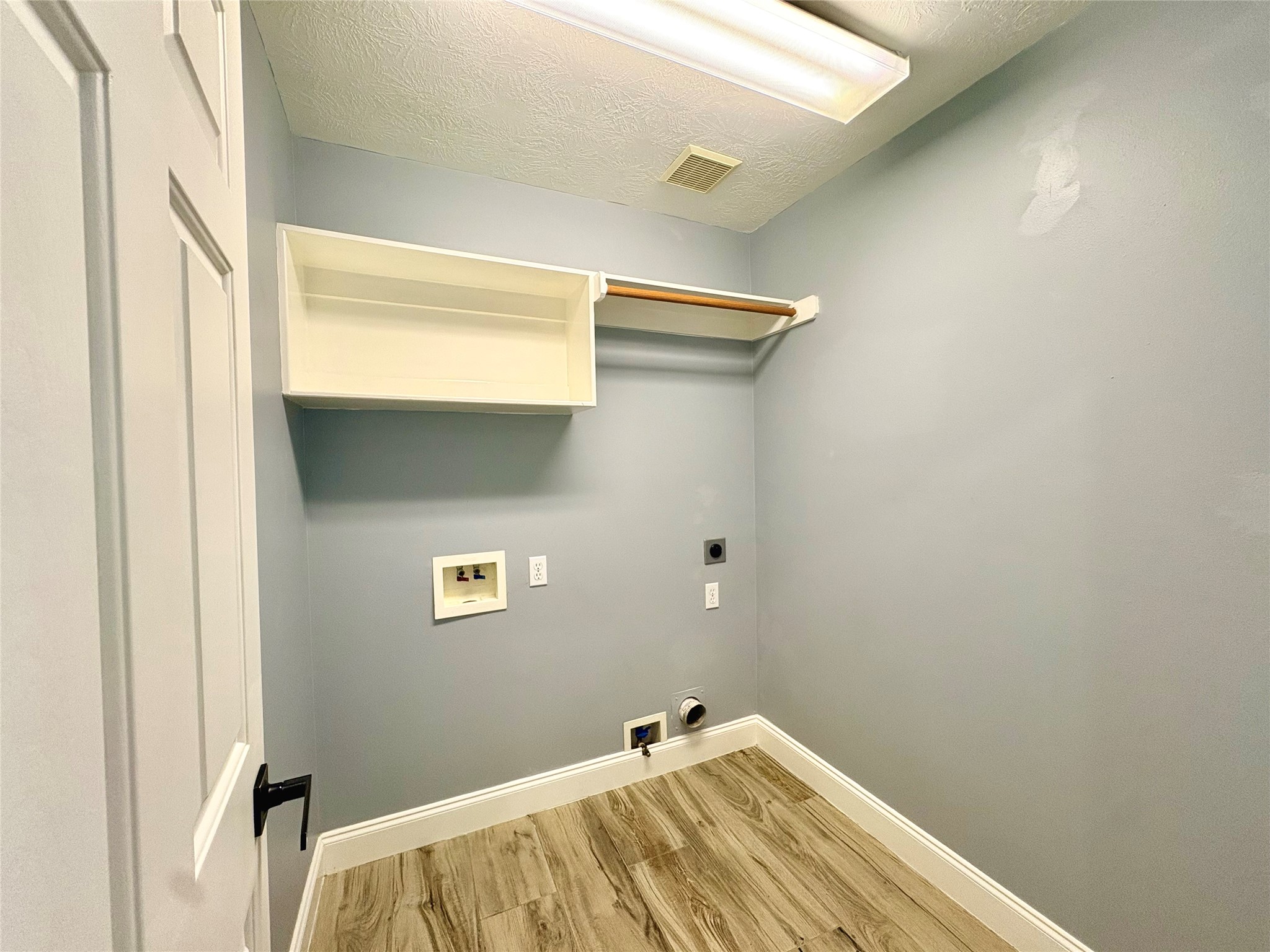 15410 Redbud Berry Way Cypress, TX 77433 - Photo 44 of 49 This is a laundry room with light blue walls, featuring hookups for a washer and dryer, a shelf, and a clothing rod. The flooring is a wood-like laminate.