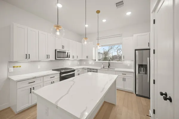 a kitchen with stainless steel appliances a stove a sink a refrigerator and white cabinets with wooden floor