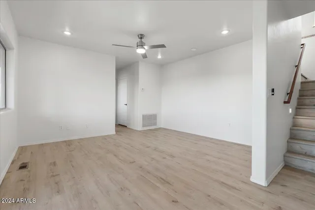 an empty room with wooden floor chandelier fan and windows