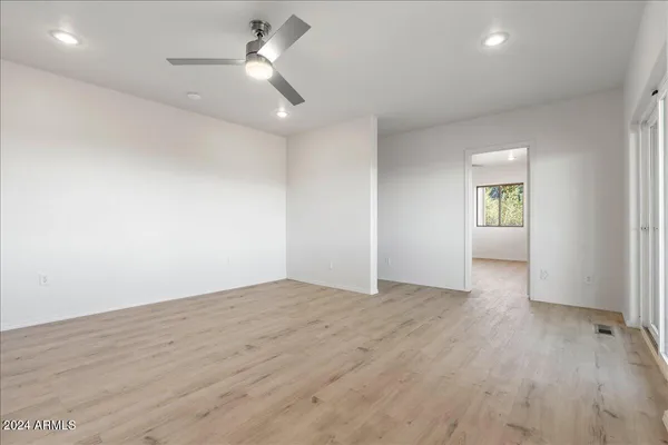 an empty room with wooden floor ceiling fan and windows
