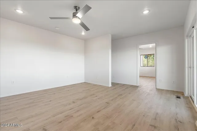 an empty room with wooden floor ceiling fan and windows