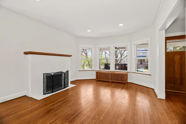 an empty room with wooden floor fireplace and windows